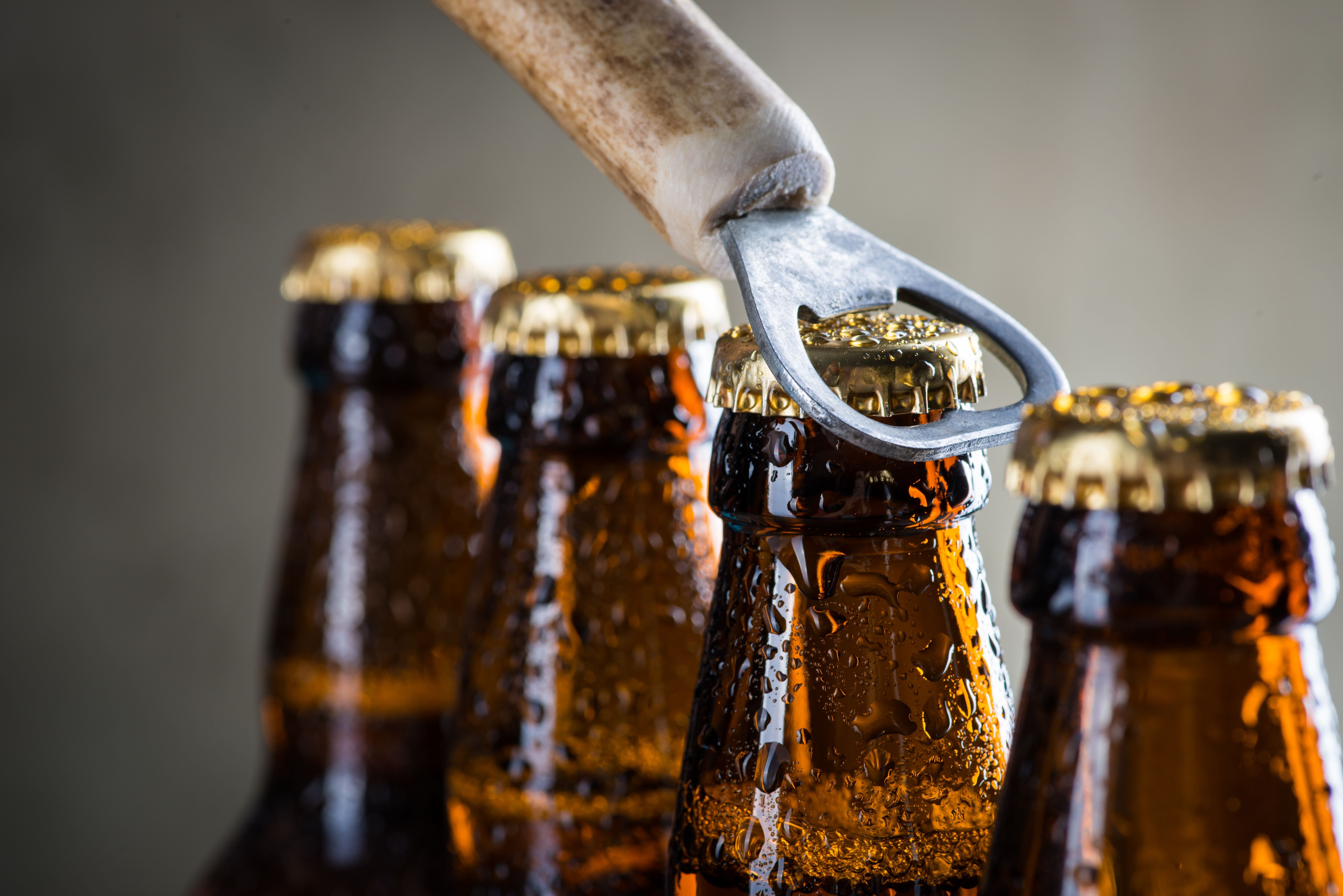 A line of brown glass beer bottles and a beer bottle opener opening a cap